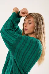 Buzo verde esmeralda tipo poncho oversize, con cuello redondo y mangas largas. Tejido de punto con ochos verticales y fondo vanizado.