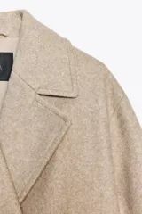 Abrigo largo color beige de cuello solapa y manga larga con trabilla y botón. Tiene bolsillos de vivo en el delantero y cierre frontal cruzado con botones.