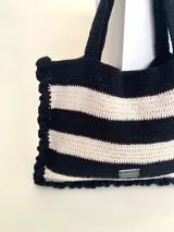 Bolso tipo tote tejido a crochet, con hilo 100% algodón, a rayas horizontales color crema y lila, con volados en los bordes y manijas reforzadas.