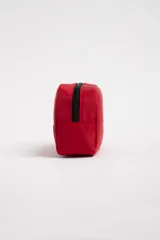 Necesser rojo rectangular de tela impermeable, con cierre superior negro, asa de mano y logo circular en relieve.