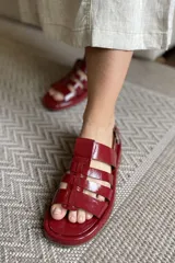 Sandalias de cuero color marrón, estilo cangrejeras, con hebilla dorada al tobillo y suela plana.