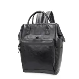 Mochila de estilo urbano, color negro, con acabado de cuero sintético (PU). Presenta dos asas superiores, correas ajustables para llevar como mochila, bolsillo frontal con cierre horizontal y bolsillos laterales abiertos. Posee un parche con el logo 'TROY' en la parte superior central.