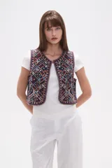 Chaleco sin mangas, sin abroches, con escote redondo. Confeccionado en tejido oscuro con bordados geométricos y florales en tonos rojos, blancos, azules y mostaza, con apliques de cuentas.