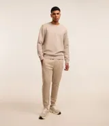 Conjunto deportivo color beige compuesto por un buzo de cuello redondo y un pantalón de jogging con cintura elástica y bolsillos laterales. El buzo es de corte clásico y el pantalón es ajustado en los tobillos.