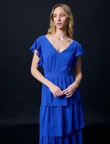 Vestido midi de gasa color azul eléctrico con estampado de lunares blancos. Tiene escote en V, mangas cortas con volados, corte en la cintura y falda escalonada con capas.