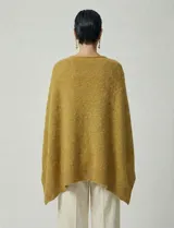 Poncho tejido de punto grueso, color mostaza/mostaza oscuro, con cuello redondo y caída amplia.
