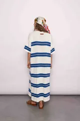 Vestido largo tejido a rayas horizontales azules y beige sobre fondo blanco, con mangas cortas y tajos laterales.