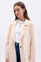 Blazer largo de mujer, color beige claro, con solapas amplias, bolsillos frontales grandes y corte recto.