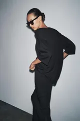 Prenda superior negra de punto liso, con cuello redondo y mangas tres cuartos. Presenta aberturas laterales en el bajo.