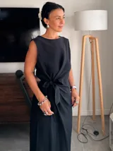 Vestido midi sin mangas, color lila pálido o gris claro, con escote redondo y detalle de lazo fruncido en la cintura que genera un drapeado en la falda.