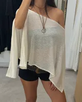 Poncho tejido color crudo, de corte asimétrico y hombro descubierto.