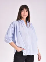 Camisa celeste con cuello mao, corte holgado, mangas 3/4 abullonadas con puños elásticos y cierre frontal con botones.