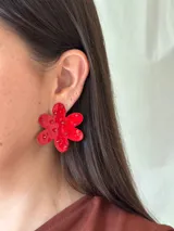 Aro grande en forma de flor de seis pétalos, color rojo brillante, con pequeños apliques de strass o mostacillas incrustadas en la superficie.