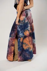 Conjunto de falda larga y top asimétrico con estampado tie-dye en tonos azul, naranja y marrón. El top es de un solo hombro y tiene un collarín con flecos dorados.