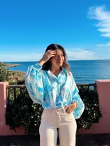 Camisa celeste con estampado abstracto, de corte amplio, cuello camisero y mangas largas abullonadas con puños elásticos.