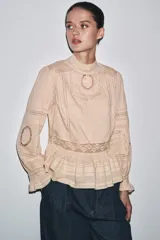 Camisa color crema de algodón con cuello alto, manga larga con puños con volantes y bordados a tono.