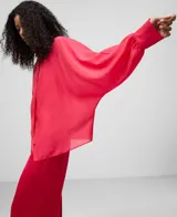 Camisa blanca de manga larga, con cuello chimenea alto y botonadura frontal oculta. El tejido es semitransparente y presenta una textura ligera.