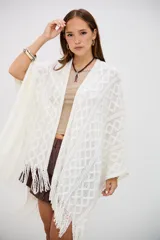 Poncho color crudo de tejido calado con diseño de rombos y flecos en el borde inferior.
