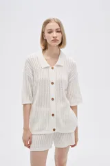 Remera de punto calado color beige, con cuello polo, mangas cortas y cierre frontal con botones.