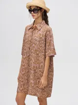 Camisa-vestido oversize de manga corta, color verde con estampado tie-dye en tonos salmón y turquesa. Presenta cuello camisero y cierre frontal de botones.