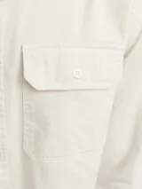 Camisa de algodón orgánico color crema, de manga larga, con cuello clásico, corte recto, cierre frontal con botones y dos bolsillos de parche en el pecho.