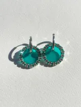 Aros colgantes con forma circular, hechos de resina color lila y borde de strass plateado. El aro es de acero quirúrgico plateado.