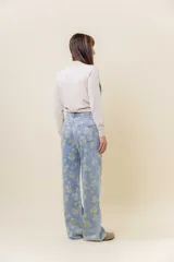 Pantalón de jean de tiro medio-alto, pierna ancha y lavado celeste claro, con estampado floral en tono amarillo pálido.