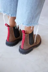 Botines Chelsea de cuero color marrón con elástico lateral negro, tirador trasero rojo y suela track negra con costuras rojas.