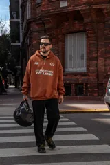 Bolso duffel negro de cuero sintético con logo de ancla bordado en rosa. Tiene doble asa de mano reforzada, correa de hombro regulable y desmontable, cierre superior con doble cremallera y tres bolsillos (dos exteriores y uno interior).