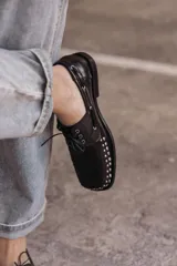 Mocasín de cuero negro con cordones y tachas metálicas en la puntera.