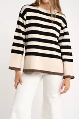 Sweater de punto a rayas horizontales negras y crudas, con cuello redondo y mangas largas. Tiene ribete marrón en puños y ruedo.