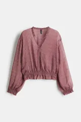 Blusa rosa con estampado floral, cuello con volados y escote en V con tiras finas para atar. Modelo de manga larga con hombros caídos y fruncido elástico con ribete de volados en puños y bajo.