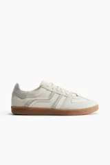 Championes deportivos color crema con detalles en gris y suela marrón. Presentan collarín acolchado, cordones y logo bordado en el lateral. Grosor de la suela 2,5 cm.