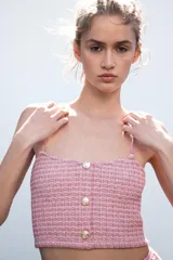Top corto rosado de tejido tweed con tirantes finos y escote recto. Cierre frontal con tres botones metálicos dorados en relieve.