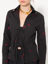 Camisa negra de poplin con bordado de chiles rojos, cierre frontal con lazos, broches decorativos dorados en el cuello y broches a presión dorados en los puños.