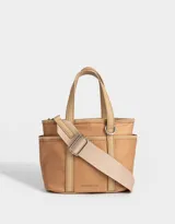 Cartera tipo tote color beige, de tela deportiva, con doble asa corta y correa larga regulable y desmontable. Tiene un bolsillo lateral con forma de pouch.