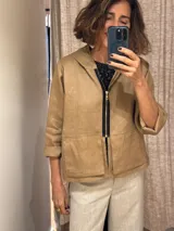 Chaqueta color beige de lino, con capucha, cierre frontal con cremallera negra, bolsillos laterales y mangas 3/4.