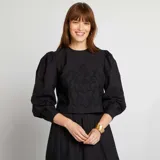 Blusa corta negra con bordado floral, mangas largas abullonadas y cuello redondo.