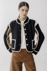 Chaqueta corta de lana color negro con detalles en beige y marrón. Tiene cuello mao, cierre frontal con botones y bolsillos de parche.