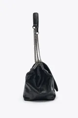 Bolso de hombro marrón oscuro de cuero sintético, con solapa y cierre magnético. Tiene un asa de cadena plateada y tres compartimentos internos, uno de ellos con cierre de cremallera.