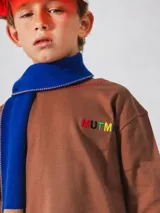 Bufanda azul y marrón con pompones grises, confeccionada en algodón.