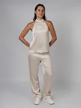 Blusa color crema de poliéster con textura plisada, cuello alto y corte sin mangas. Presenta cierre de botón y ojo de cerradura en la parte posterior del cuello y bajo con acabado ondulado.