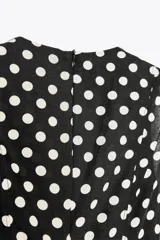 Vestido midi negro con estampado de lunares blancos, cuello redondo y sin mangas.