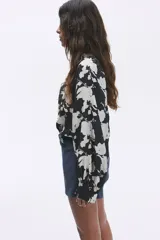 Blusa oversized con cuello elevado fruncido, abertura en V adelante y bajo recto. Mangas globo largas de corte raglán con abertura y botón en los puños.