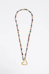 Collar largo compuesto por pequeñas piedras semipreciosas de colores variados (tonos pastel, verdes, azules, rojos) engarzadas en hilo, con un dije colgante de corazón calado con acabado metálico mate dorado.