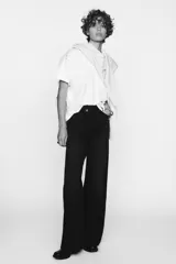 Pantalón de jean celeste de tiro alto, corte wide leg y largo hasta el tobillo. Presenta un diseño asimétrico en la cintura con cierre frontal cruzado con cremallera y botones metálicos.