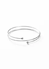 Brazalete plateado de acero quirúrgico hipoalergénico, con diseño abierto y ajustable, y terminaciones en forma de esfera.