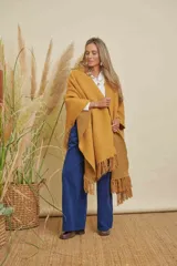 Ruana tejida color mostaza con terminación en flecos de lana y espalda en forma de V.