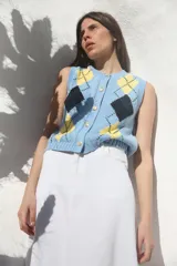 Chaleco celeste de punto con patrón de rombos en amarillo y negro, cuello redondo y cierre frontal con botones dorados.