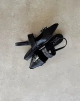 Chatas de cuero vacuno color negro, con punta fina, tira sobre el empeine con hebilla metálica y tira trasera con elástico.